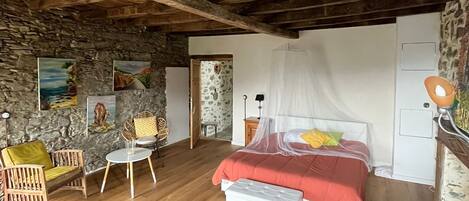 A rustic bedroom with exposed wooden beams, a stone wall, a bed with a canopy, a small table, and a chair.