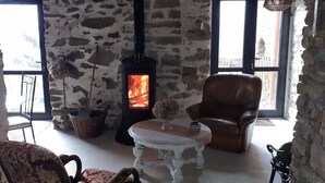 Una habitación con paredes de piedra, chimenea, sillón de cuero y una pequeña mesa con un jarrón.
