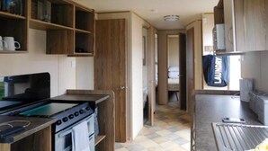 A compact kitchen with wooden cabinets, a stove, and a laundry area. - Lynch Lane Lodge - Relax in Weymouth (Weymouth)