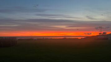A sunset over a grassy field with a distant view of a body of water and a few buildings.