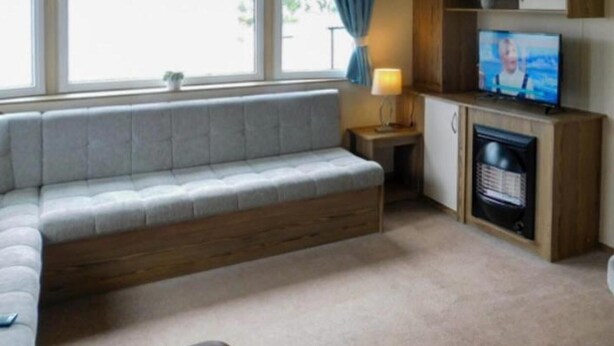 A living room with a sofa, a television, a fireplace, and a window with curtains. - Lynch Lane Lodge - Relax in Weymouth (Weymouth)