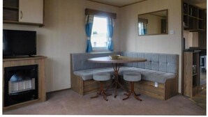 A compact living space with a sofa, a small round table, a television, and a fireplace. - Lynch Lane Lodge - Relax in Weymouth (Weymouth)