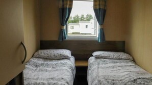 A small room with two beds, a window with curtains, and a view of a building outside. - Lynch Lane Lodge - Relax in Weymouth (Weymouth)