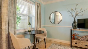 A room with a round table, two chairs, a TV on a stand, a mirror, and a vase with branches. - Sunny Retreat: Cozy APT in WPB #2 (West Palm Beach)