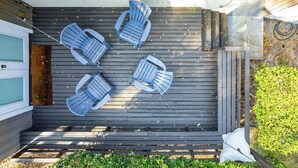 A deck with four Adirondack chairs and a white pillow, surrounded by a wooden deck and a small garden area.