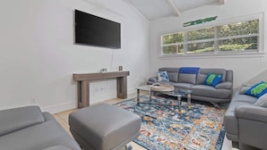 A modern living room with a flat-screen TV, grey sofas, a coffee table, and a patterned rug.