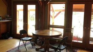 Une salle à manger en bois avec une table ronde et quatre chaises, de grandes fenêtres et un luminaire suspendu.