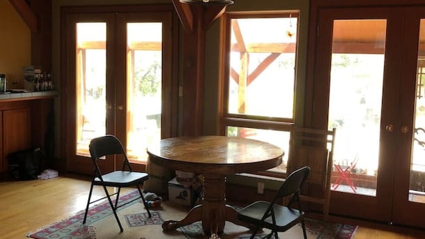 Ein Esszimmer mit Holzboden, einem runden Tisch und vier Stühlen, großen Fenstern und einer Pendelleuchte.