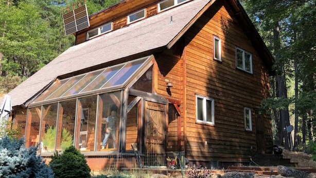 Une cabane en bois avec un toit en pente, de grandes fenêtres et une véranda couverte.