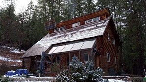 Eine Holzhütte mit geneigtem Dach, umgeben von schneebedeckten Bäumen und einem klaren Himmel.