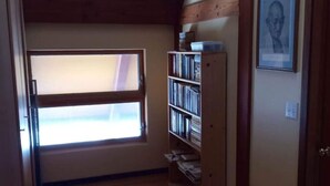 Une pièce avec un plafond en pente, des poutres en bois, une fenêtre et une bibliothèque.