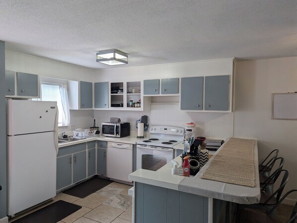 A compact kitchen with white appliances, blue cabinets, and a small dining area with a table and chairs. - Charming 2-bedroom townhome in Summerton with WiFi and AC (Summerton)