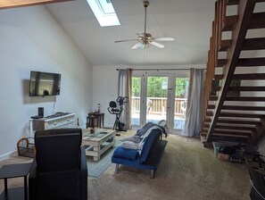 A spacious living room with a ceiling fan, a television, a sofa, and a staircase leading to an outdoor deck. - Charming 2-bedroom townhome in Summerton with WiFi and AC (Summerton)
