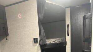 A compact RV interior with a bunk bed, a small seating area, and a kitchenette. - “RV Country Living” Glamping (Clewiston)