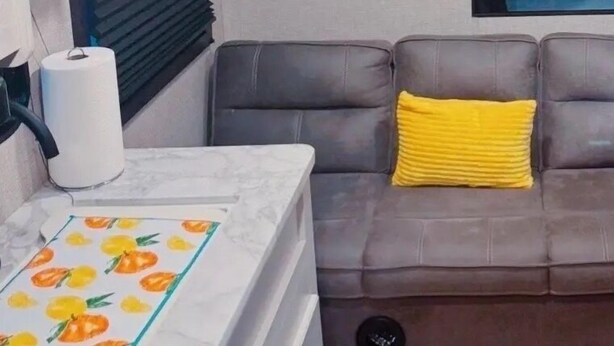 A compact living space with a kitchenette, a sofa with a yellow pillow, and a bed with a headboard. - “RV Country Living” Glamping (Clewiston)