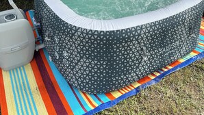 A portable hot tub with a geometric pattern, placed on a colorful striped mat beside a white RV. - “RV Country Living” Glamping (Clewiston)