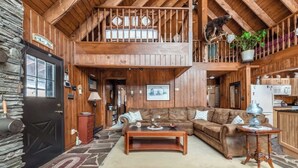 A rustic cabin interior with a wooden ceiling, a stone wall, a black door, a living room with a sofa and coffee table, and a kitchen area. - The Luxury Cabin at Deep Hollow (Narrowsburg)