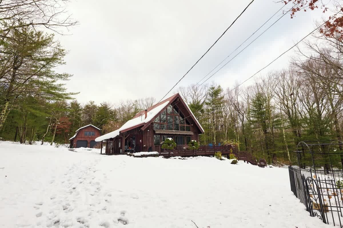 Een chalet met een grote glazen voorgevel, omringd door besneeuwde grond en bomen.