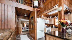 A wooden cabin interior with a stone floor, a white refrigerator, wooden cabinets, a kitchen counter, and a dining area. - The Luxury Cabin at Deep Hollow (Narrowsburg)