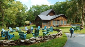 A lodge with a stone wall, outdoor seating, and a barbecue grill. - The Luxury Cabin at Deep Hollow (Narrowsburg)