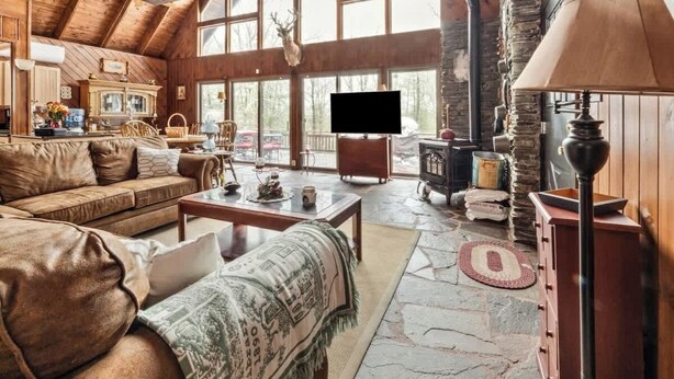 A cozy living room with a fireplace, a television, and a stone floor. - The Luxury Cabin at Deep Hollow (Narrowsburg)