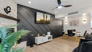 A modern living room with a white console table, a mounted TV, and a dining area with a white table and black chairs.
