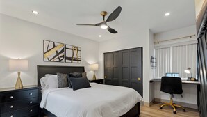 A modern bedroom with a bed, bedside tables, a desk, and a ceiling fan.