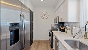 A modern kitchen with stainless steel appliances, a marble backsplash, and white cabinetry.