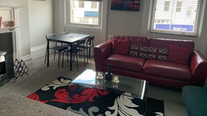 A living room with a red leather sofa, a glass coffee table, a dining table with chairs, and a TV mounted on the wall. - Perfect Location next to bars & restaurants and 10 mins walk to Bournemouth pier (Bournemouth)