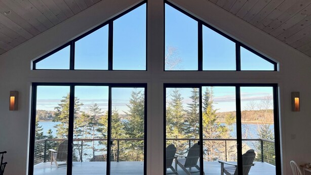 Ein geräumiges Zimmer mit großen Fenstern und Blick auf einen See und Bäume.