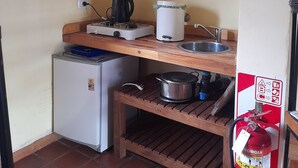 Una cocina compacta con estufa a gas, refrigerador blanco, pileta y estante de madera.