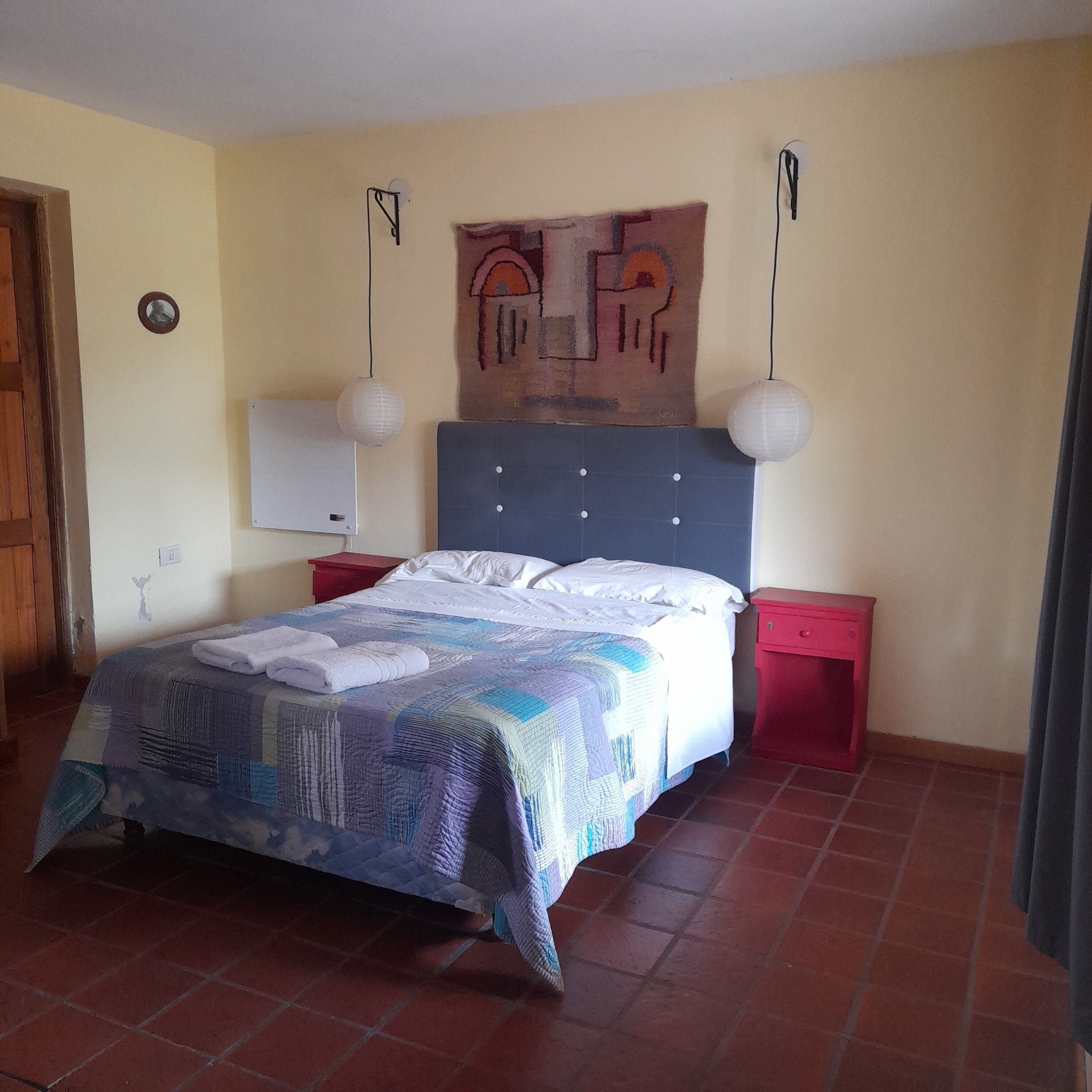 A bedroom with a bed, two nightstands, a wall clock, and a painting.