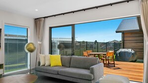 A modern living room with a grey sofa, a round coffee table, and a large window overlooking a wooden deck. - Stylish New Retreat in Taupo (Taupo)