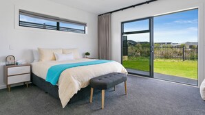 A bedroom with a large bed, a nightstand, a bench, and a sliding glass door leading to a balcony. - Stylish New Retreat in Taupo (Taupo)