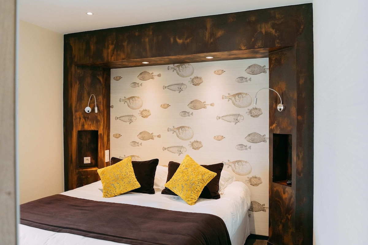 A bedroom with a bed, two pillows, a wall with fish wallpaper, and a wooden headboard.