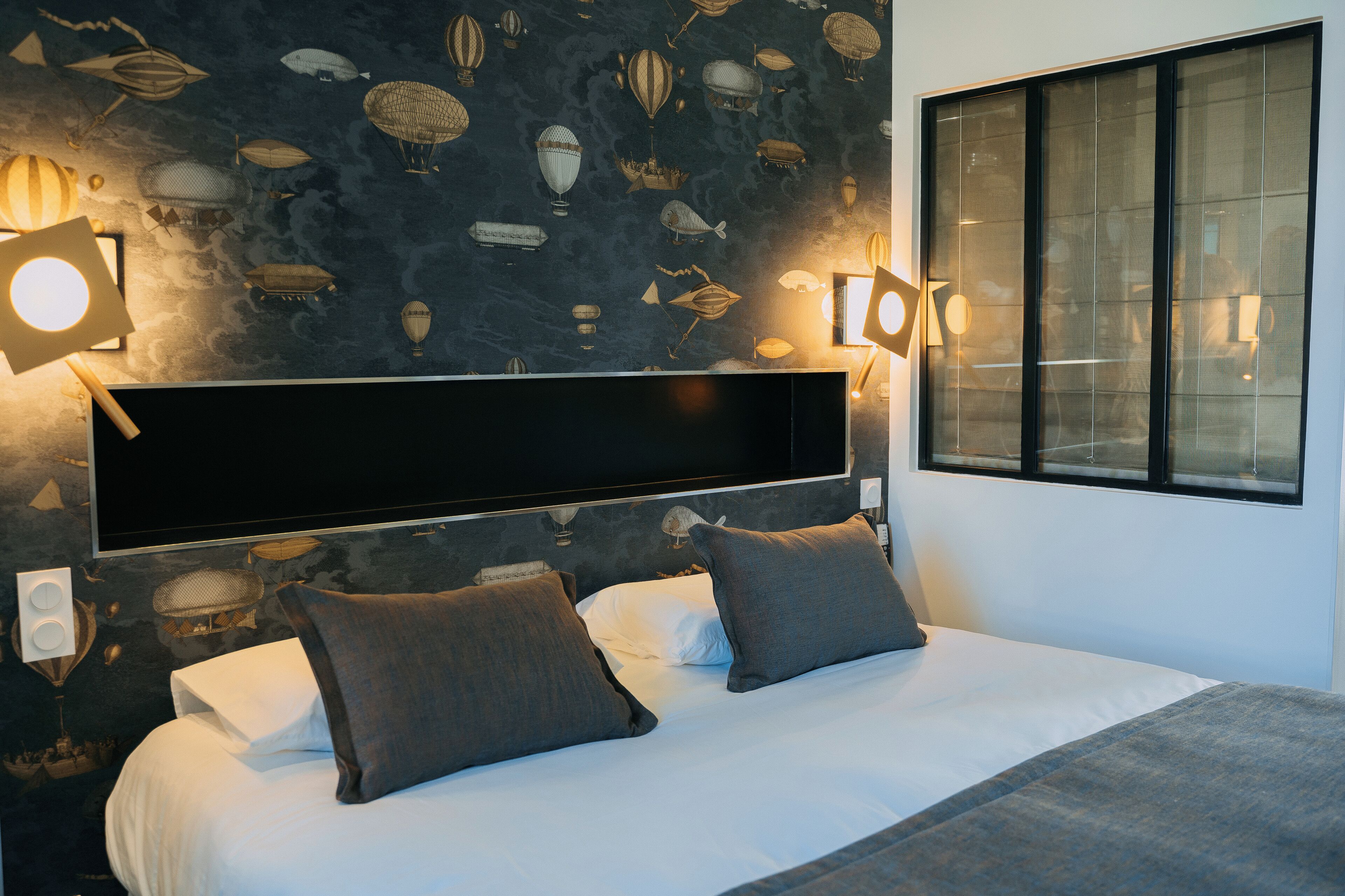 A modern bedroom with a large bed, two bedside lamps, and a wall mural of hot air balloons.