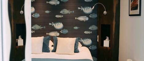 Une chambre à coucher avec un lit, des oreillers, une tête de lit ornée de motifs de poissons, des lampes de chevet et un tableau encadré accroché au mur.