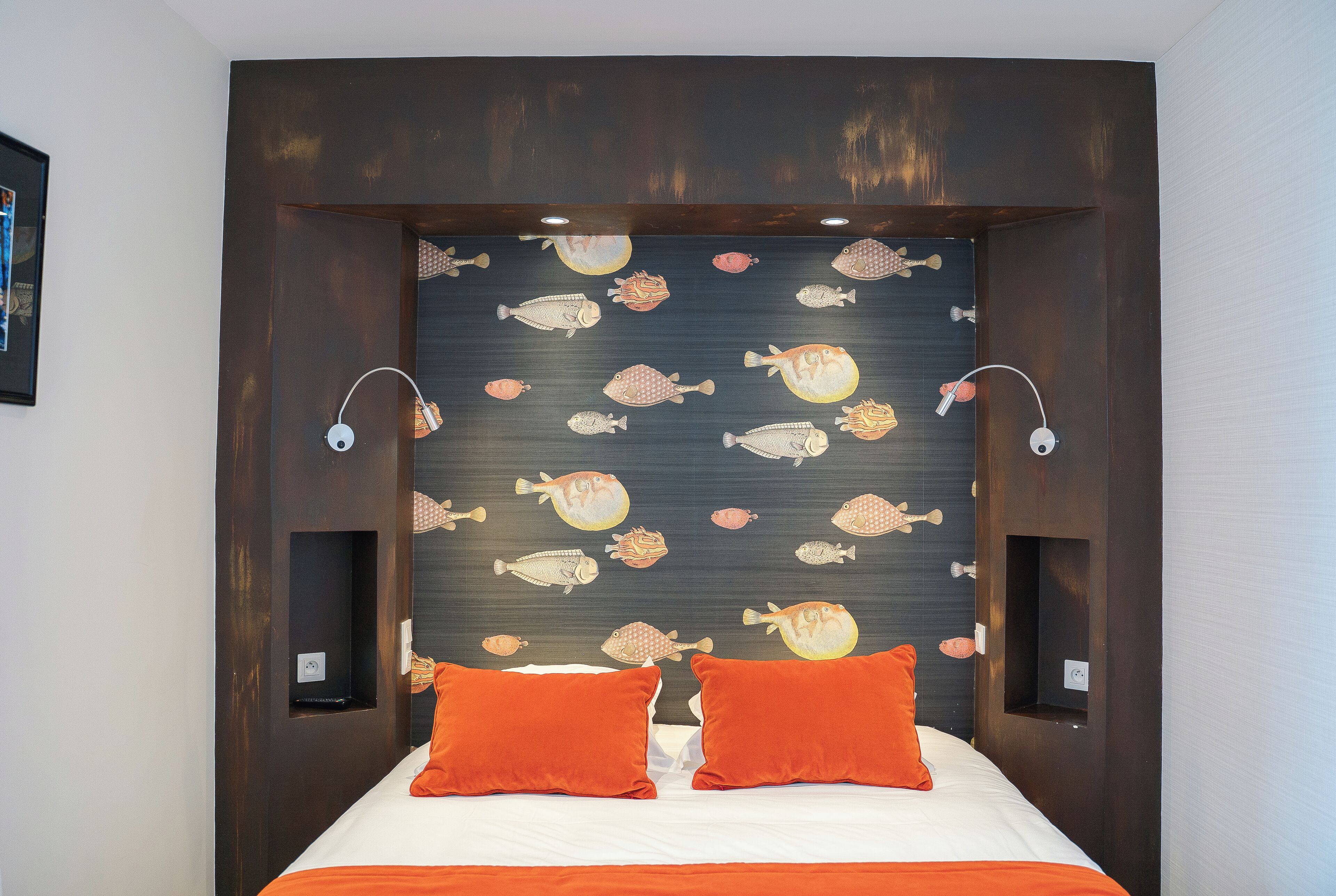 Habitació d'hotel amb un llit, almoinos taronja i una paret amb motius de peixos.
