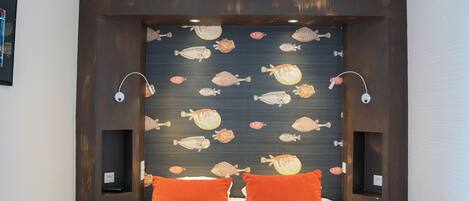 Habitació d'hotel amb un llit, almoinos taronja i una paret amb motius de peixos.