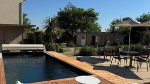 A poolside area with wooden decking, lounge chairs, and a small table. - les agapanthes (Ploubazlanec)