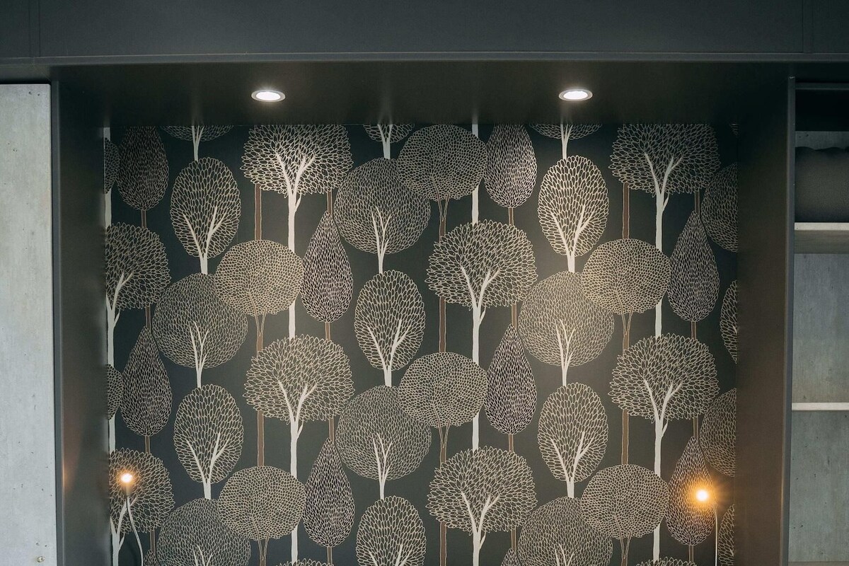 Une chambre à coucher avec un lit, deux oreillers et un mur décoré d’un motif d’arbre.