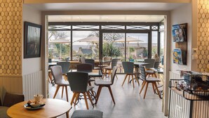 A café with tables and chairs, a view of the outside, and a wall-mounted menu board. - les agapanthes (Ploubazlanec)