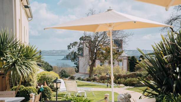 A patio area with outdoor seating, a view of the sea, and a building in the background. - les agapanthes (Ploubazlanec)