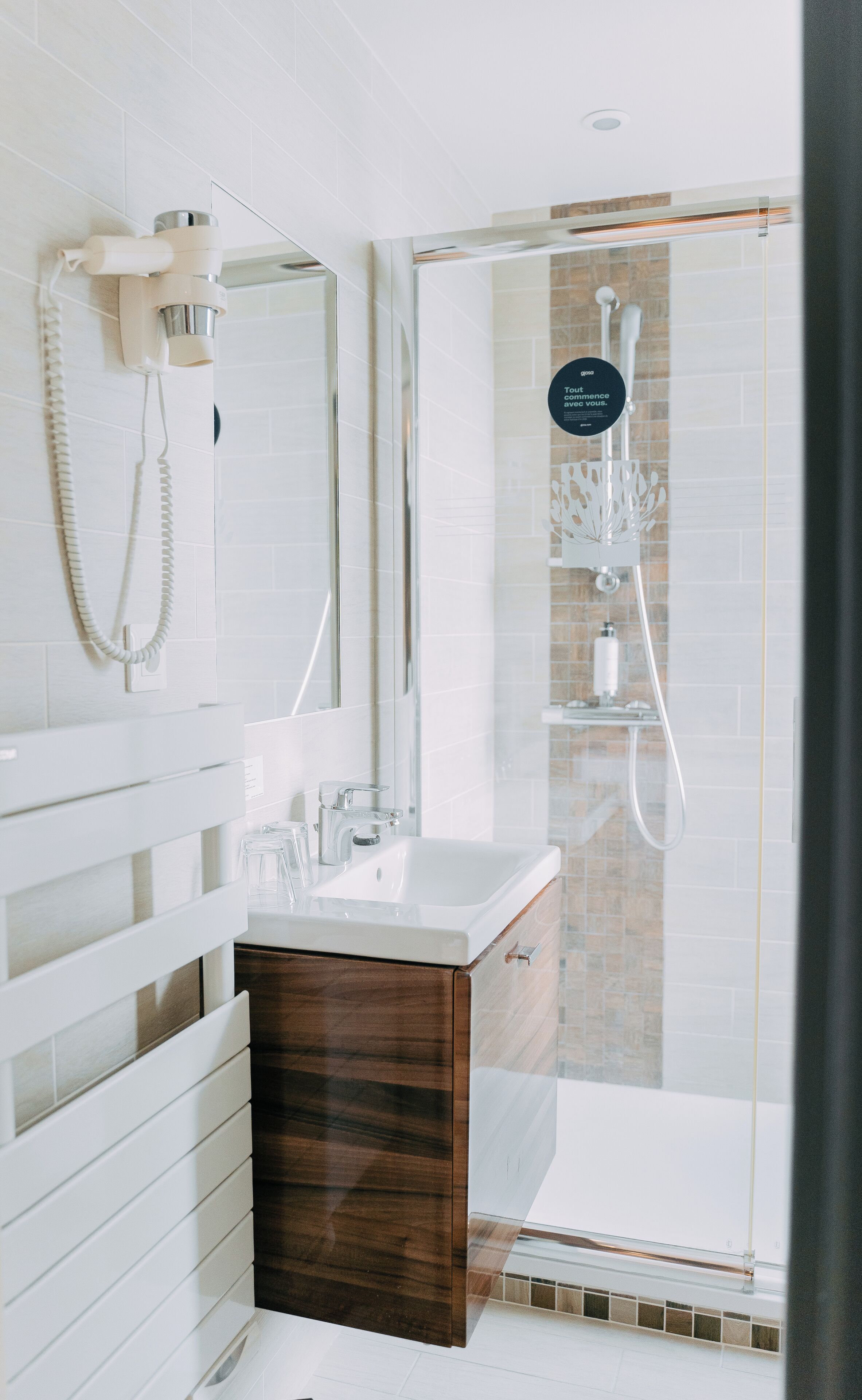 A modern bathroom with a glass shower enclosure, a white sink, and a wooden vanity.