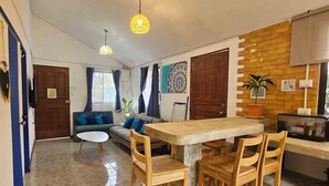 Een ruime woonkamer met een houten eettafel en stoelen, een bank met blauwe kussens en een decoratief wandobject.