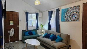 Een woonkamer met een bank, twee fauteuils, een salontafel, een ventilator en een decoratief wandobject.