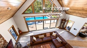 Un salón amplio con un sofá de cuero marrón grande, una mesa de centro de madera y vistas a una piscina a través de amplios ventanales.