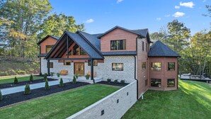 A modern log cabin with a stone facade, a large deck, and a well-maintained lawn. - Lazaj Luxury Lodge — Heated Pool,Hot Tub, Game Room,Sleeps 16 Near Hocking Hills (Logan)