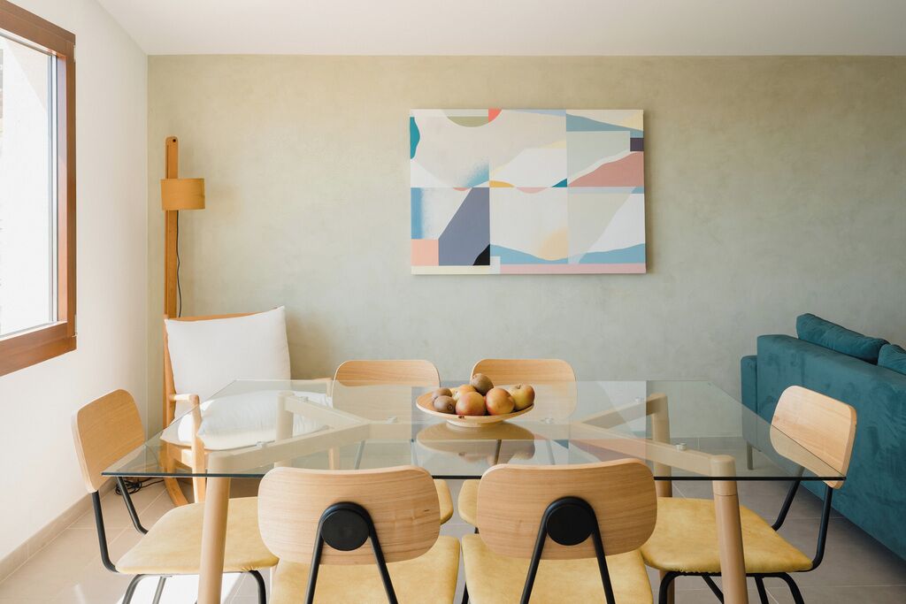 Un comedor moderno con una mesa de vidrio, sillas de madera y un cuenco de fruta.