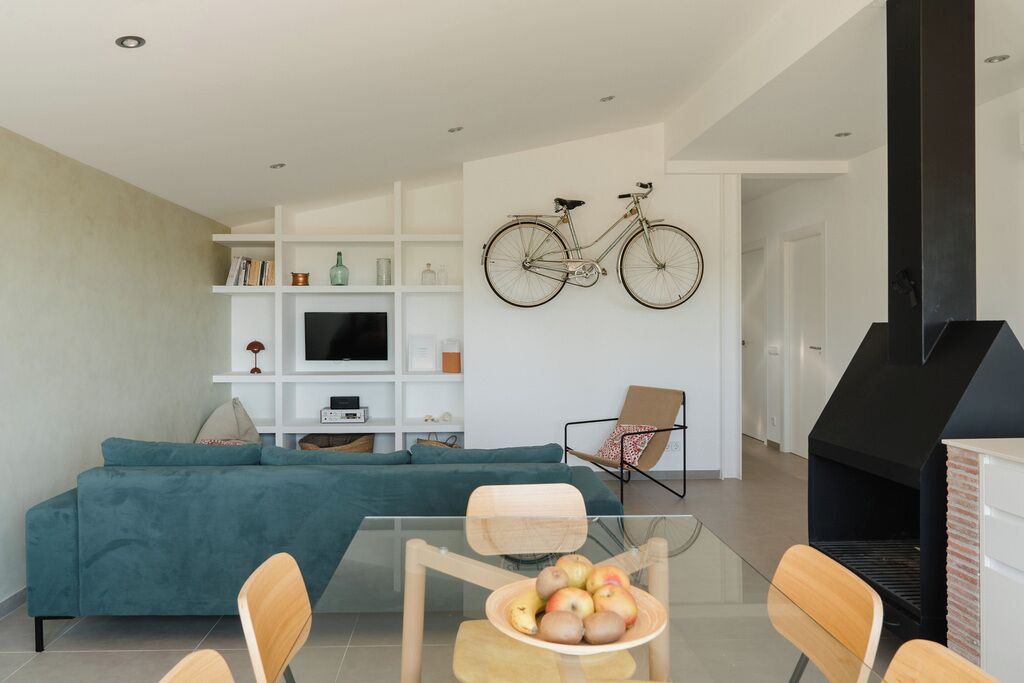 A modern living room with a teal sofa, a glass dining table with chairs, a mounted bicycle, and a black fireplace.